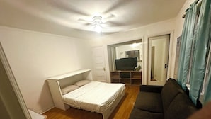 Habitación compacta con cama, sofá, televisor y ventilador de techo.
