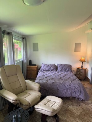 A bedroom with a bed, a chair, a lamp, and a small table.