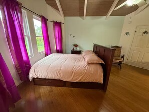 Une chambre à coucher avec un lit en bois, une table de chevet, une chaise et une fenêtre avec des rideaux.