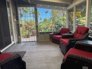 A room with wicker furniture, a glass door leading outside, and a view of greenery.