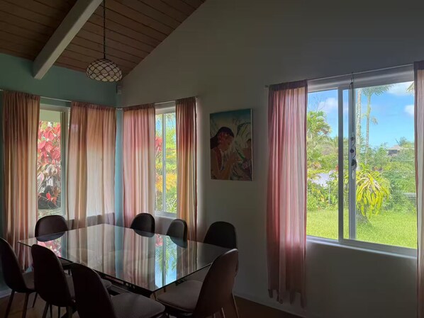 A conference room with a glass table and chairs, large windows with curtains, and a painting on the wall.