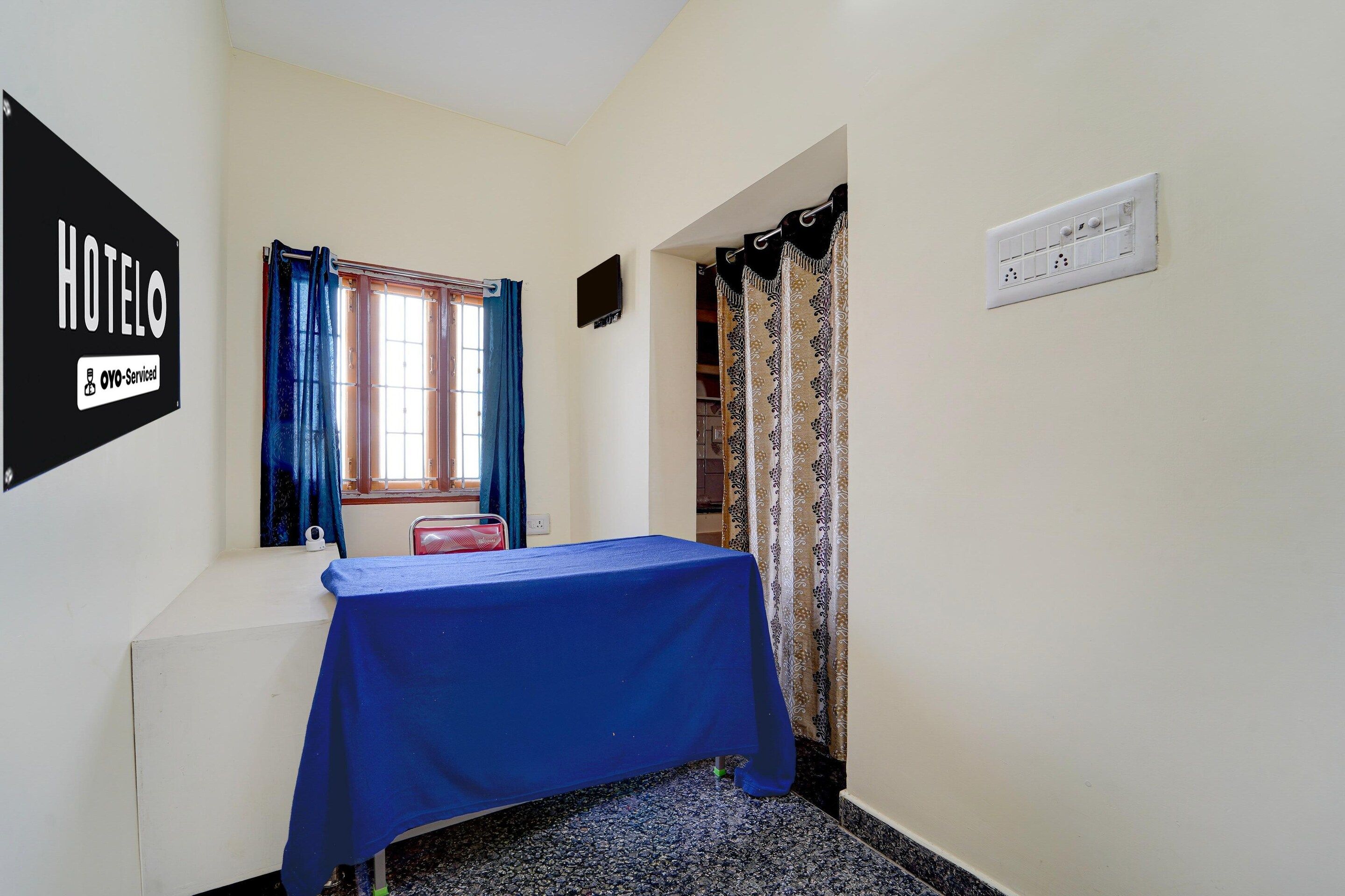 Quarto de hotel pequeno e individual, com cama, janela com cortinas, televisão na parede e tomada.