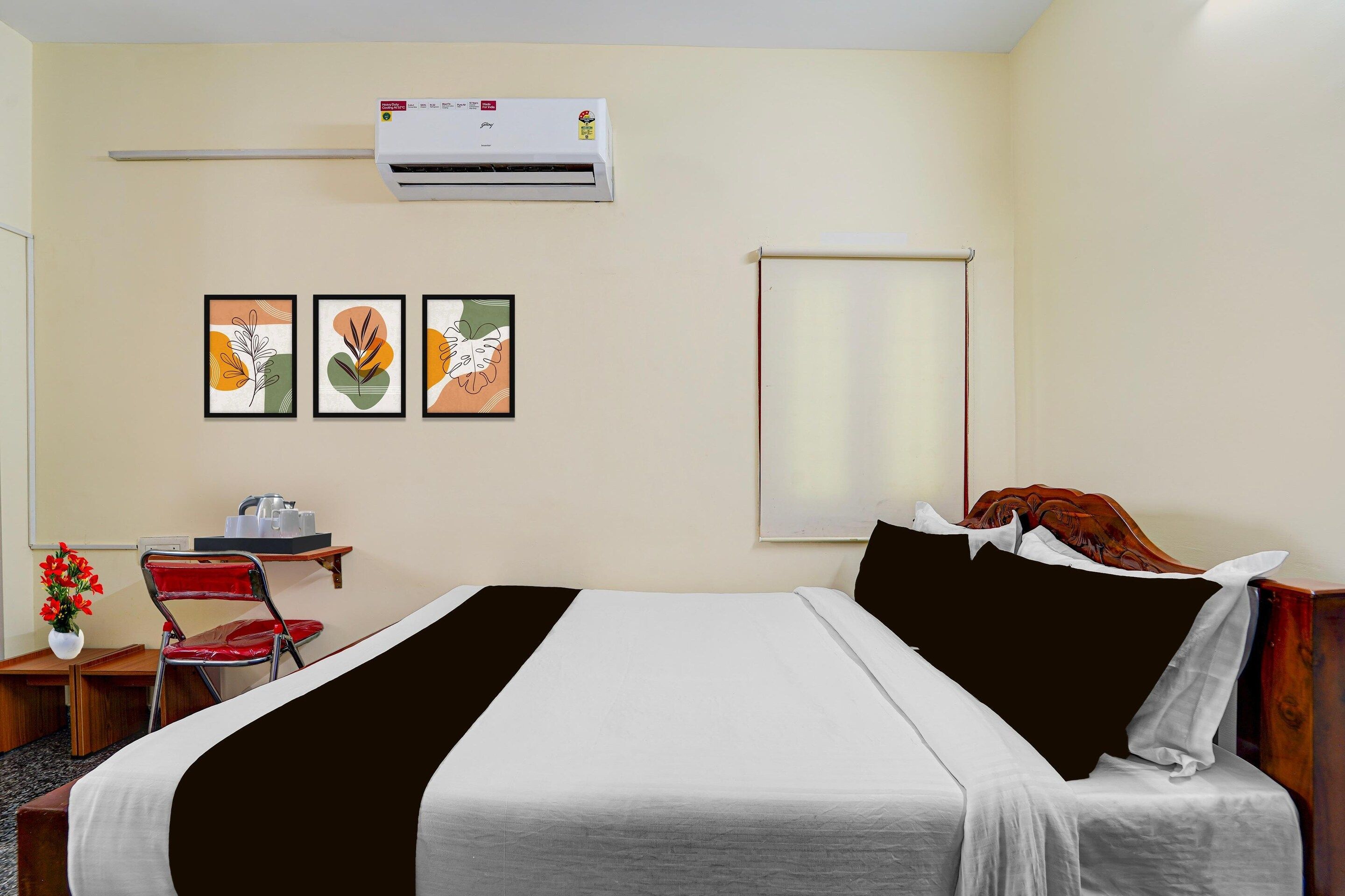 Une chambre d’hôtel comprenant un lit, un bureau avec une chaise, un climatiseur et trois œuvres d’art encadrées accrochées au mur.
