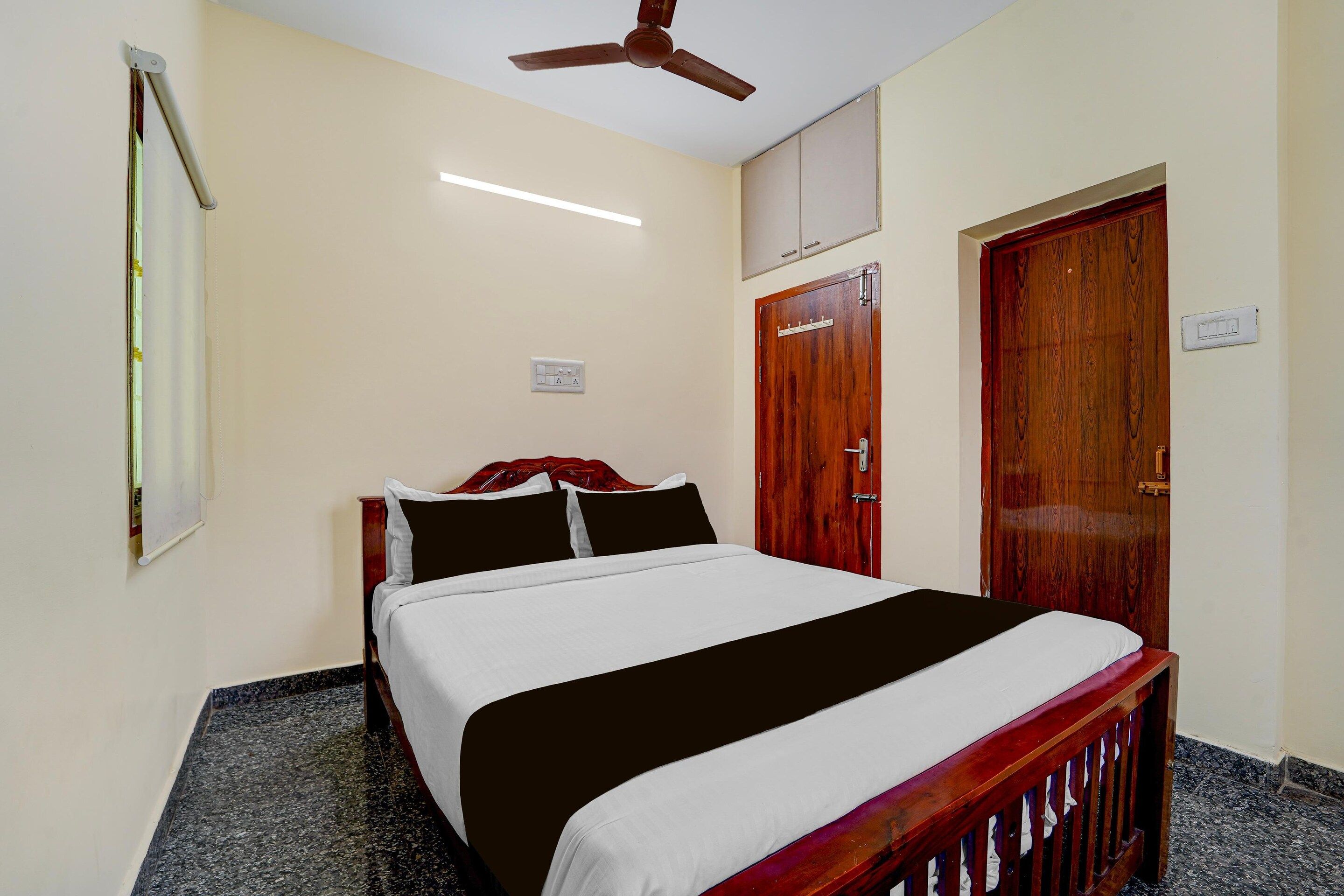 Un dormitorio con una cama, un ventilador de techo, una puerta de madera y un interruptor de luz en la pared.