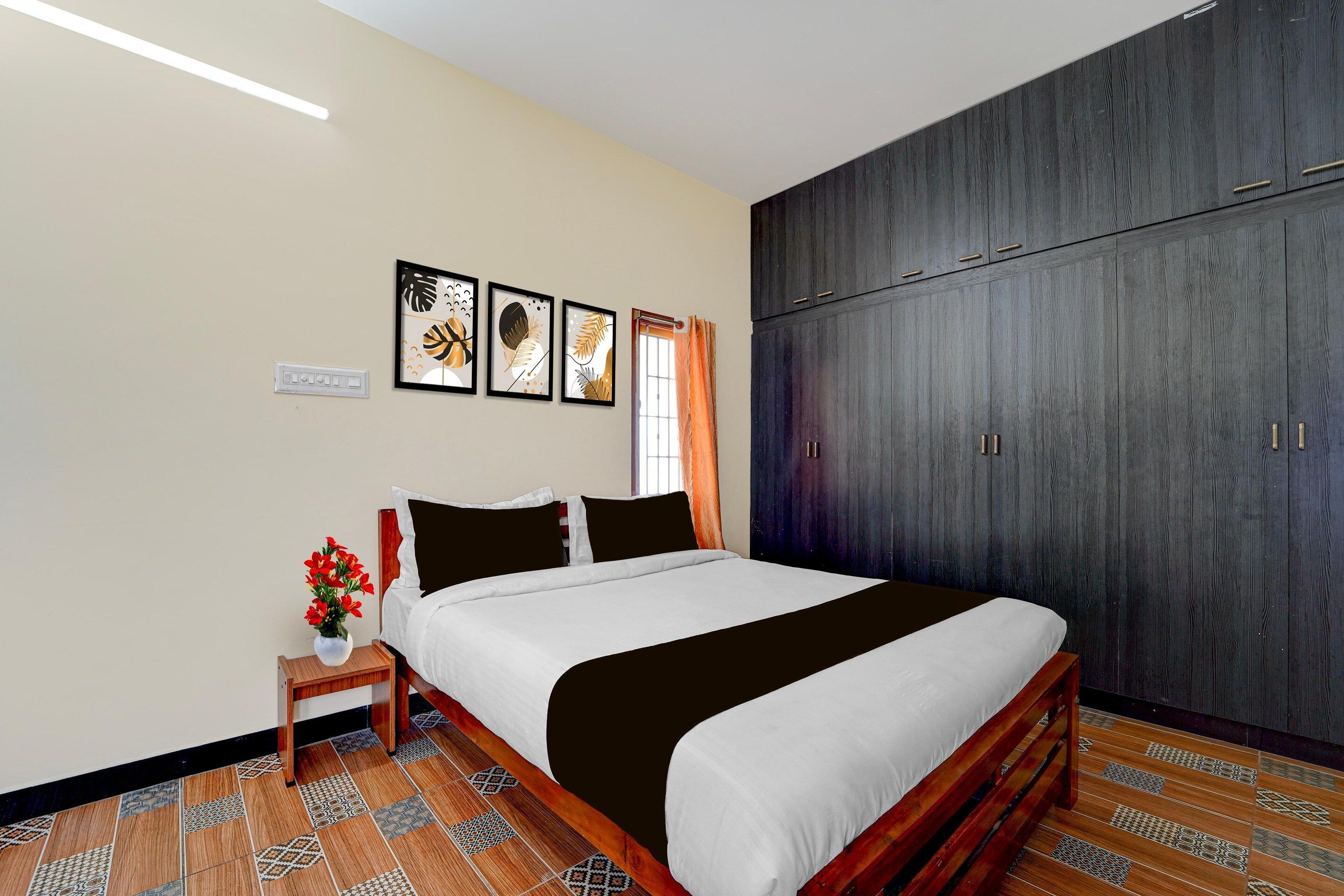 A bedroom with a bed, a nightstand, a vase with flowers, a wardrobe, and a window with curtains.