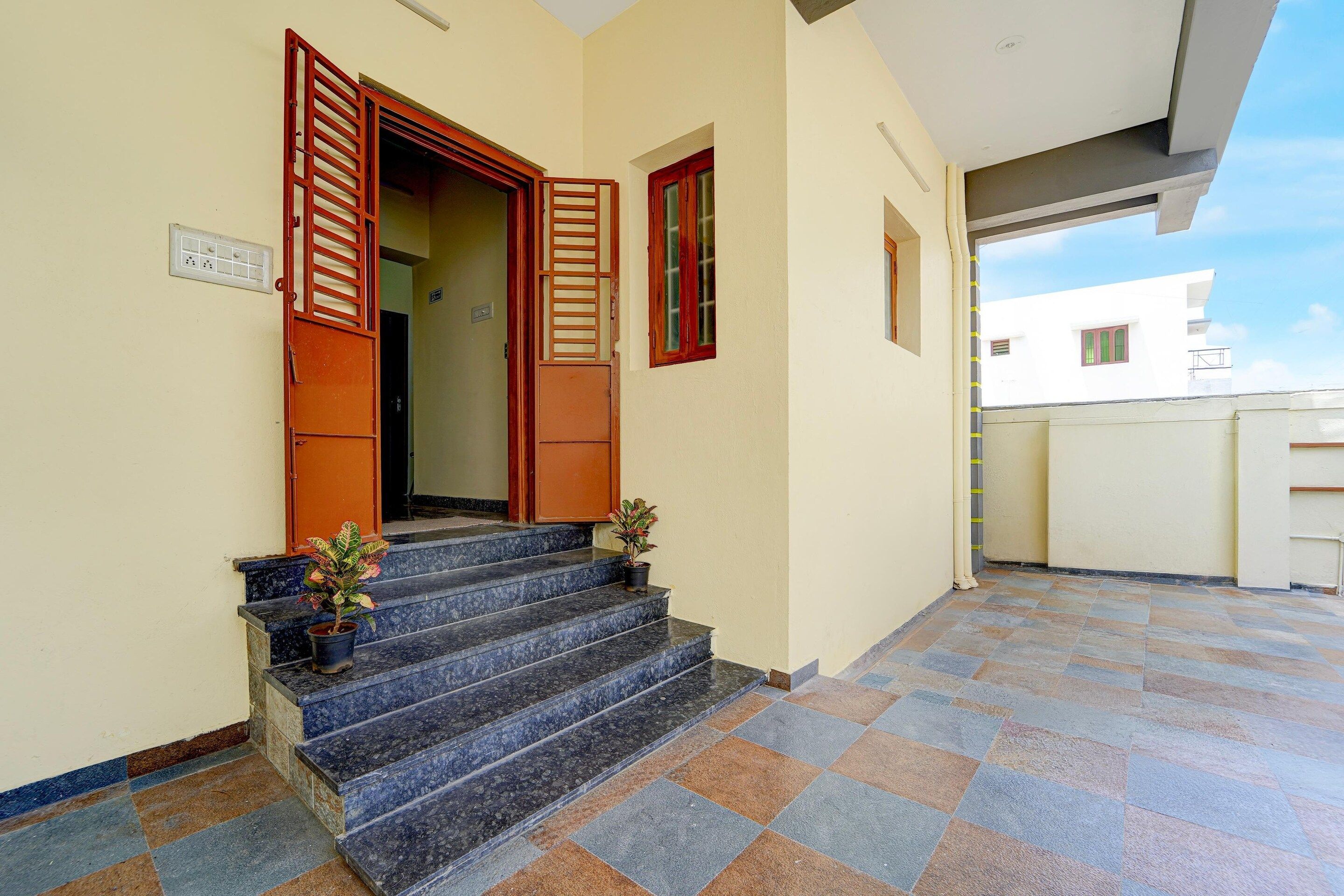 Entrada de um edifício com um conjunto de degraus levando a uma porta, um vaso de planta nos degraus e piso de azulejos.