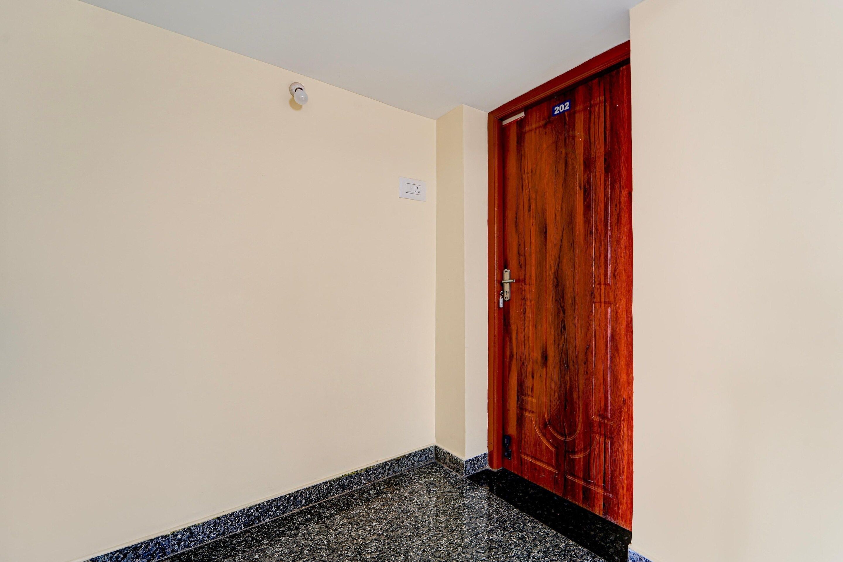 A hallway with a wooden door marked '202' and a light switch on the wall.