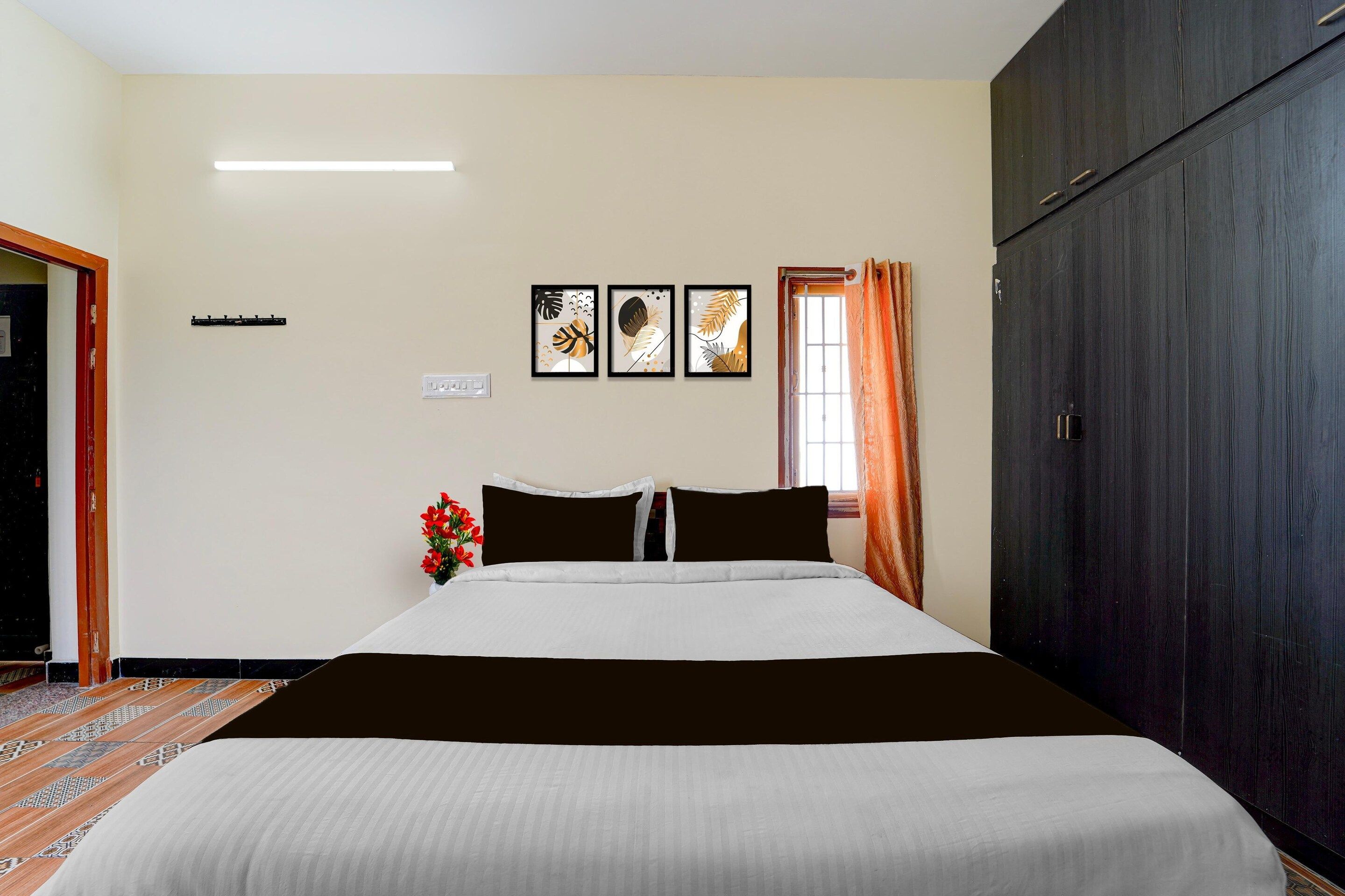 Quarto de hotel com cama, guarda-roupa, janela com cortinas e três quadros na parede.