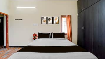 Quarto de hotel com cama, guarda-roupa, janela com cortinas e três quadros na parede.