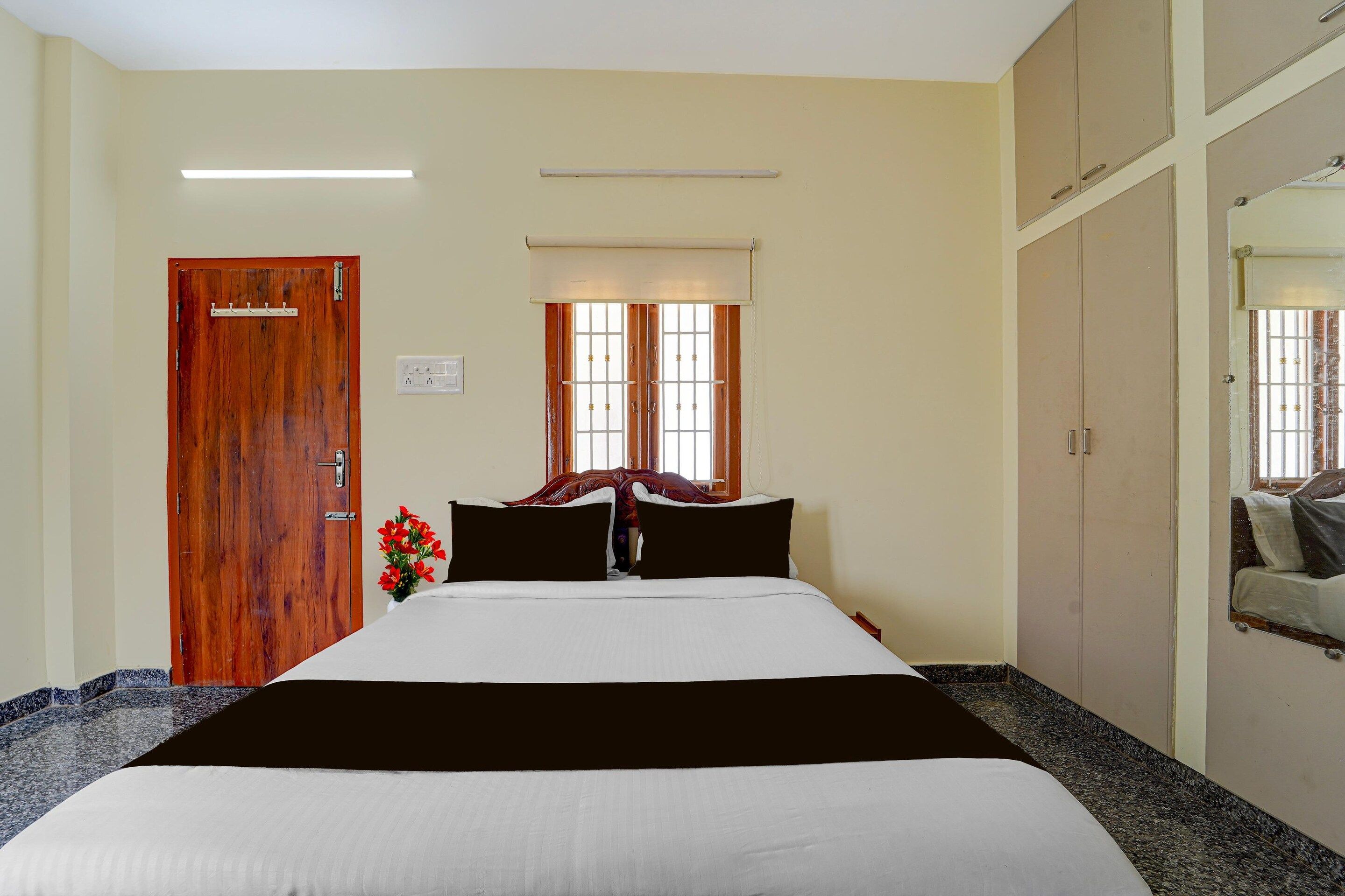 Une chambre à coucher avec un lit, une porte en bois, une fenêtre avec des stores, un miroir et un luminaire fixé au mur.