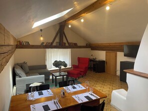 A loft-style room with a dining area, a red chair, a sofa, and a television. - Plaz Aldier, (Sent) by Interhome (Sent)
