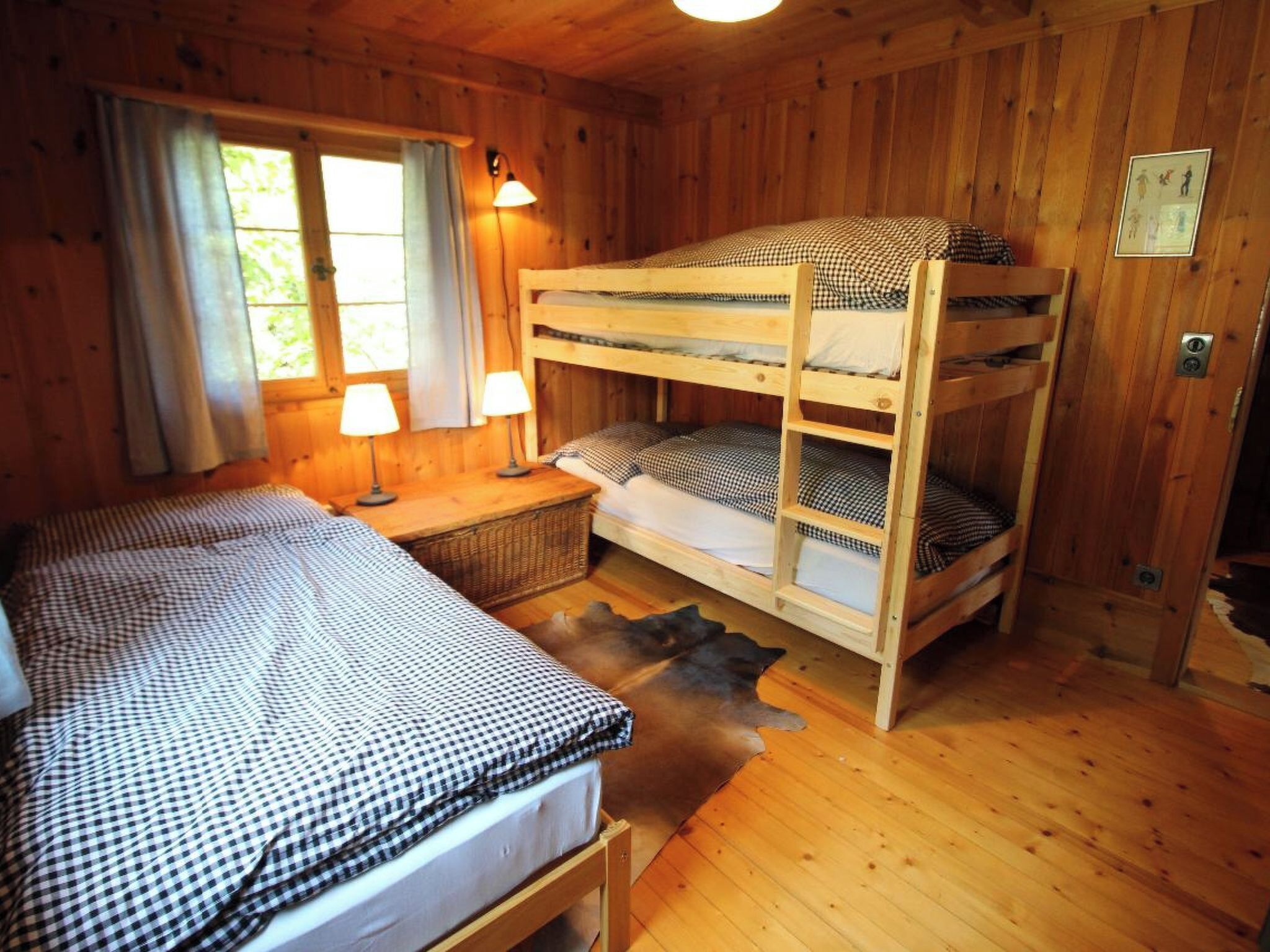 Une chambre de cabane en bois avec des lits superposés, un lit simple, une table de chevet avec des lampes et une fenêtre avec des rideaux.