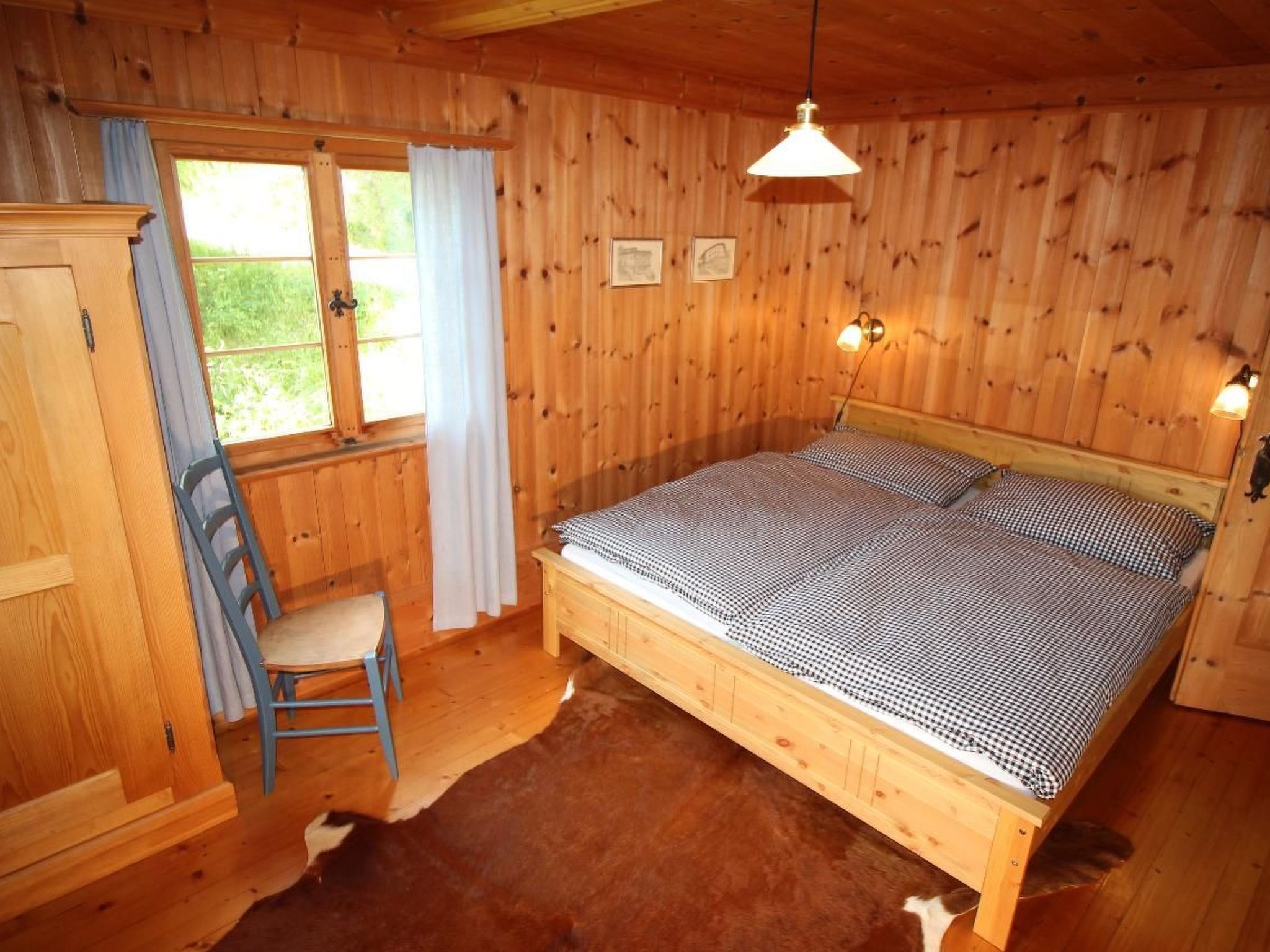 Une pièce en bois avec un lit, une chaise, une fenêtre avec des rideaux et des lampes fixées au mur.