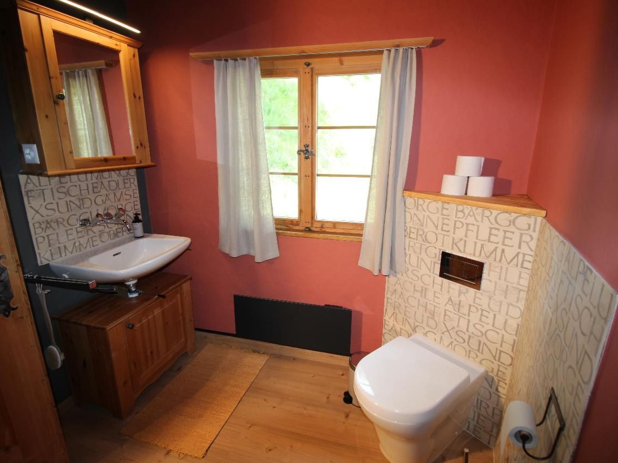 A bathroom with a wooden cabinet, a sink, a toilet, and a window with curtains.