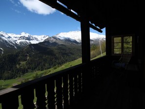 A room with a view of snow-capped mountains, a wooden balcony, and a window with a chair. - Ferienhaus Chas'alba, (Sta. Maria Val Müstair) by Interhome (Sta. Maria GR)