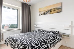A bedroom with a bed, a window with curtains, a view of buildings, and a painting on the wall. - Serene Top-Floor Retreat with Lake Views in Järfälla (Järfälla)