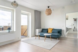Moderni olohuone, jossa on sohva, kaksi sivupöytää, riippuvalaisin ja näkymä suuresta ikkunasta.