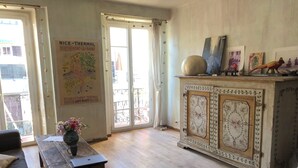 A room with a wooden floor, a vintage cabinet, a sofa, a table with a vase, and a poster on the wall.
