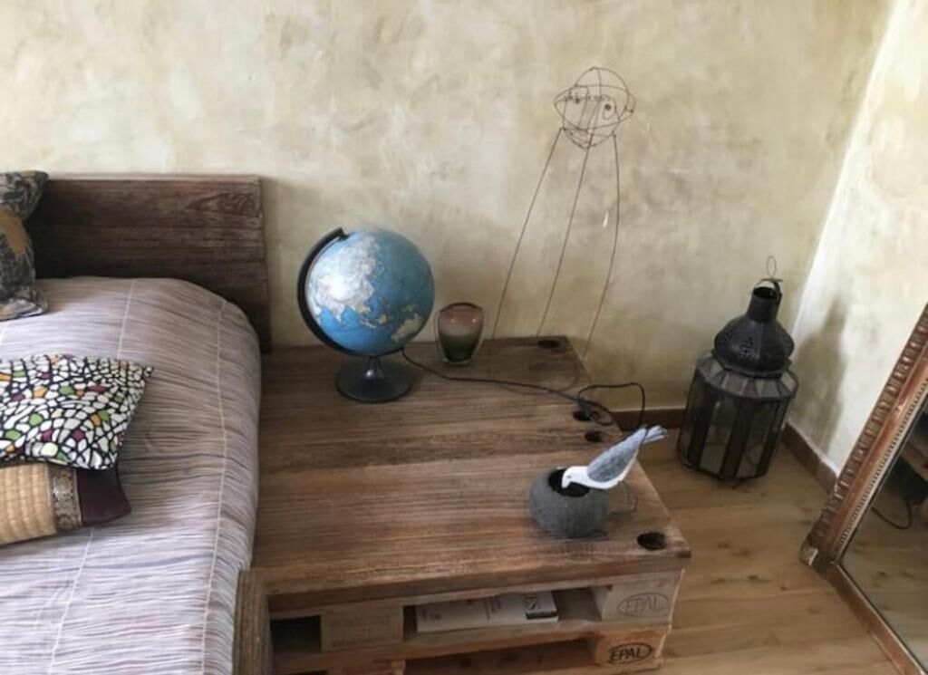 Una mesita de noche de madera con un globo terráqueo, una lámpara y un pequeño florero con una figurita de pájaro.