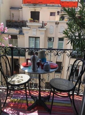 A balcony with a round table and two chairs, a striped rug, and a view of a building with balconies and windows.