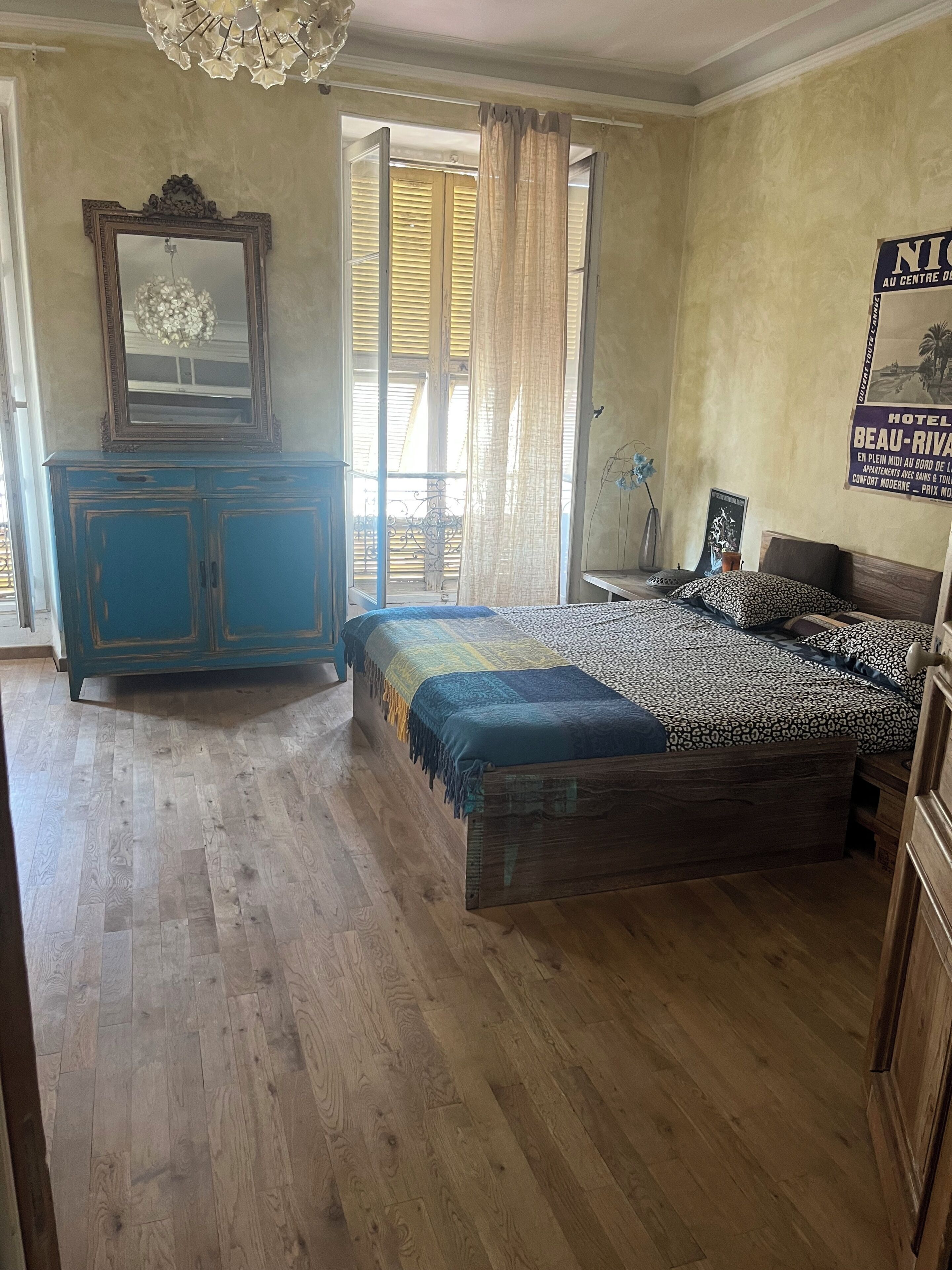 Une chambre à coucher avec un lit, une commode, un miroir et une fenêtre avec des rideaux.