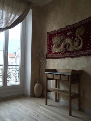 A room with a wooden floor, a table, a vase with branches, and a wall tapestry with a dragon design.