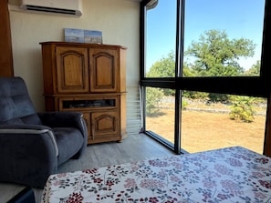 A room with a large window, a wooden cabinet, a grey sofa, and a floral bedspread.