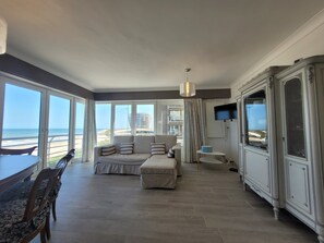 A spacious living area with a sofa, a dining table, and a TV mounted on the wall. - Apartment With Panoramic Sea Views (Middelkerke)