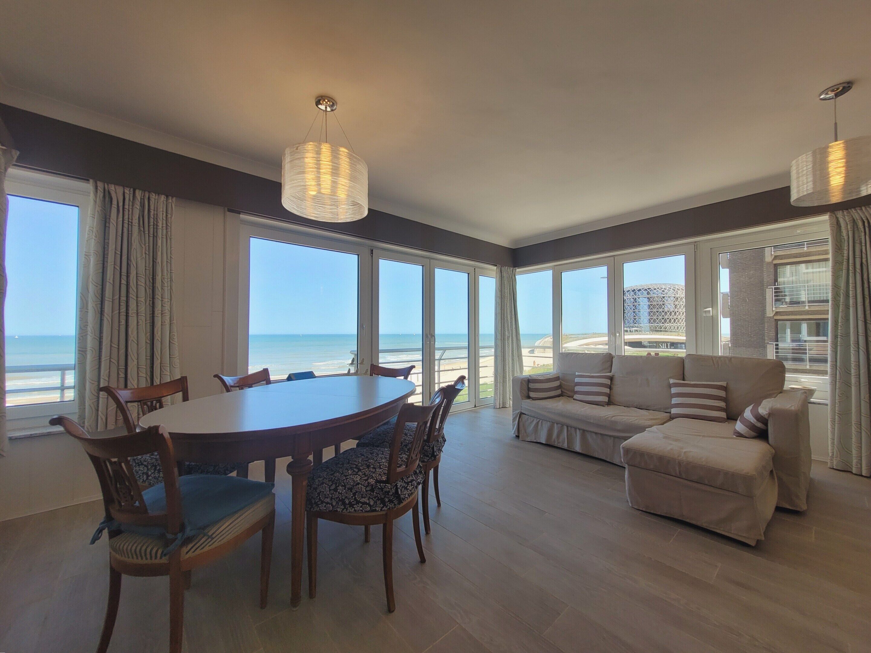 Un vaste espace de vie comprenant un coin repas avec une table, des chaises et un canapé, donnant sur une plage.
