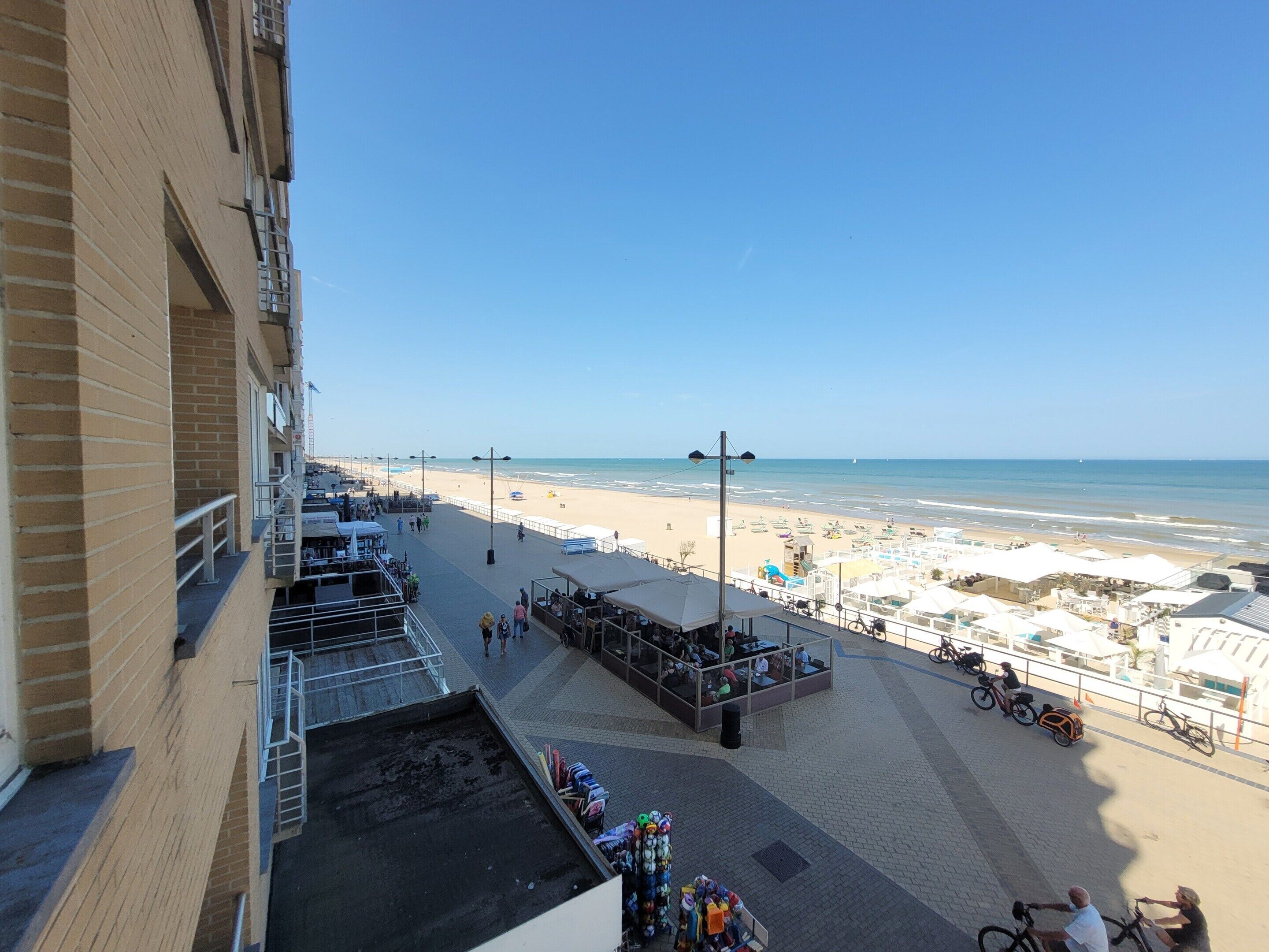 Un paseo marítimo frente a la playa, con vista despejada al mar, una zona de descanso cubierta y un carril bici.