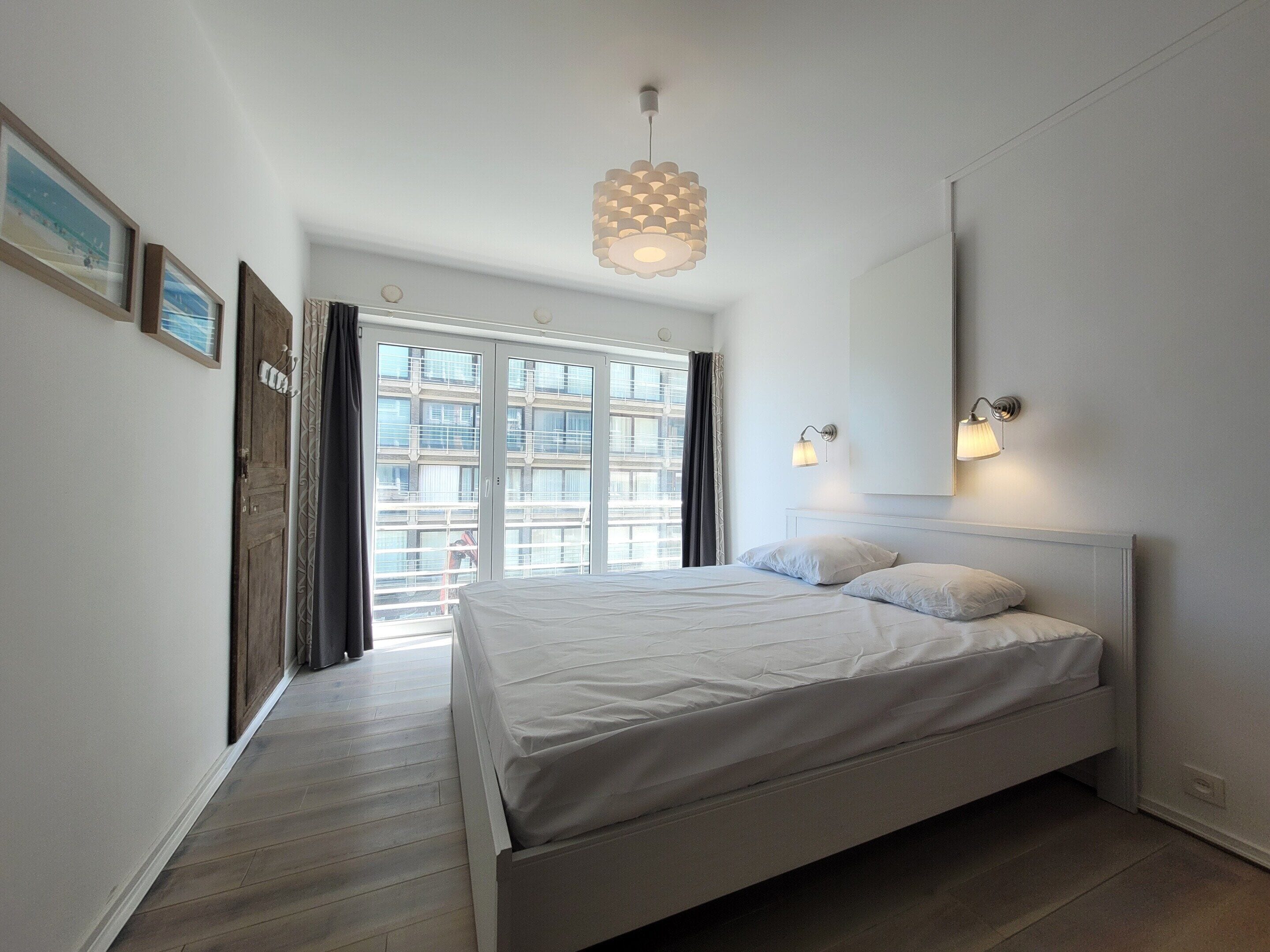 Un dormitorio con cama, un ventanal grande y una lámpara colgante.
