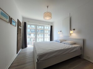 A bedroom with a bed, a large window, and a pendant light. - Apartment With Panoramic Sea Views (Middelkerke)