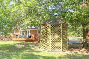Ein Gazebo mit Gitterwerk, umgeben von Gras und Bäumen.