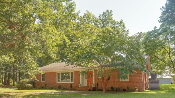 A single-story brick house with a front porch, a small garden, and a tall tree in front. - Back Deck, Grill, Yard! New Bern Family Home (New Bern)