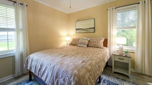 A bedroom with a bed, a nightstand, a ceiling fan, and a window with curtains. - Back Deck, Grill, Yard! New Bern Family Home (New Bern)