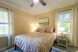 Ein Schlafzimmer mit einem Bett, einem Nachttisch, einem Deckenventilator und einem Fenster mit Vorhängen.
