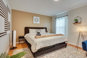A neatly arranged bedroom with a bed, bedside table, lamp, and a potted plant. - Easy NYC Commute: Furnished Jersey City Home (Jersey City)