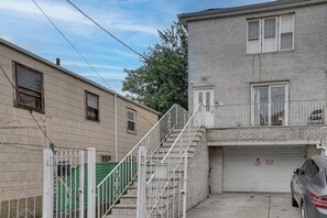 A residential building with a two-story structure, a front staircase, a garage, and a parked car. - Easy NYC Commute: Furnished Jersey City Home (Jersey City)