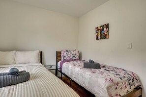 A bedroom with two beds, a wooden headboard, a small table, and a wall-mounted artwork. - Easy NYC Commute: Furnished Jersey City Home (Jersey City)