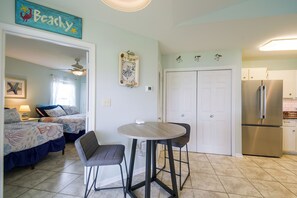 Un espace de vie compact comprenant un coin cuisine, un coin repas avec une table et des chaises, et une chambre à coucher avec un lit et une table de chevet.
