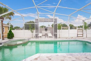 A swimming pool with a covered area, two lounge chairs, and a small tree. - 3BR 2BA Pool Home Near Disney and FL Attractions (Davenport)