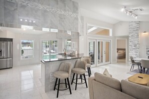 A modern kitchen with a central island, bar stools, and a dining area with a sofa and table. - 3BR 2BA Pool Home Near Disney and FL Attractions (Davenport)