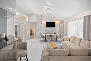 A modern living room with a sofa, a dining table, and a TV mounted on the wall. - 3BR 2BA Pool Home Near Disney and FL Attractions (Davenport)