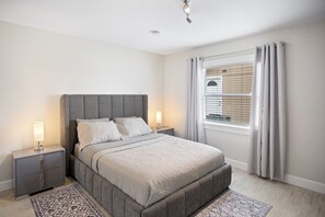 Een slaapkamer met een groot bed, twee nachtkastjes, een venster met zonwering en een plafondlamp.