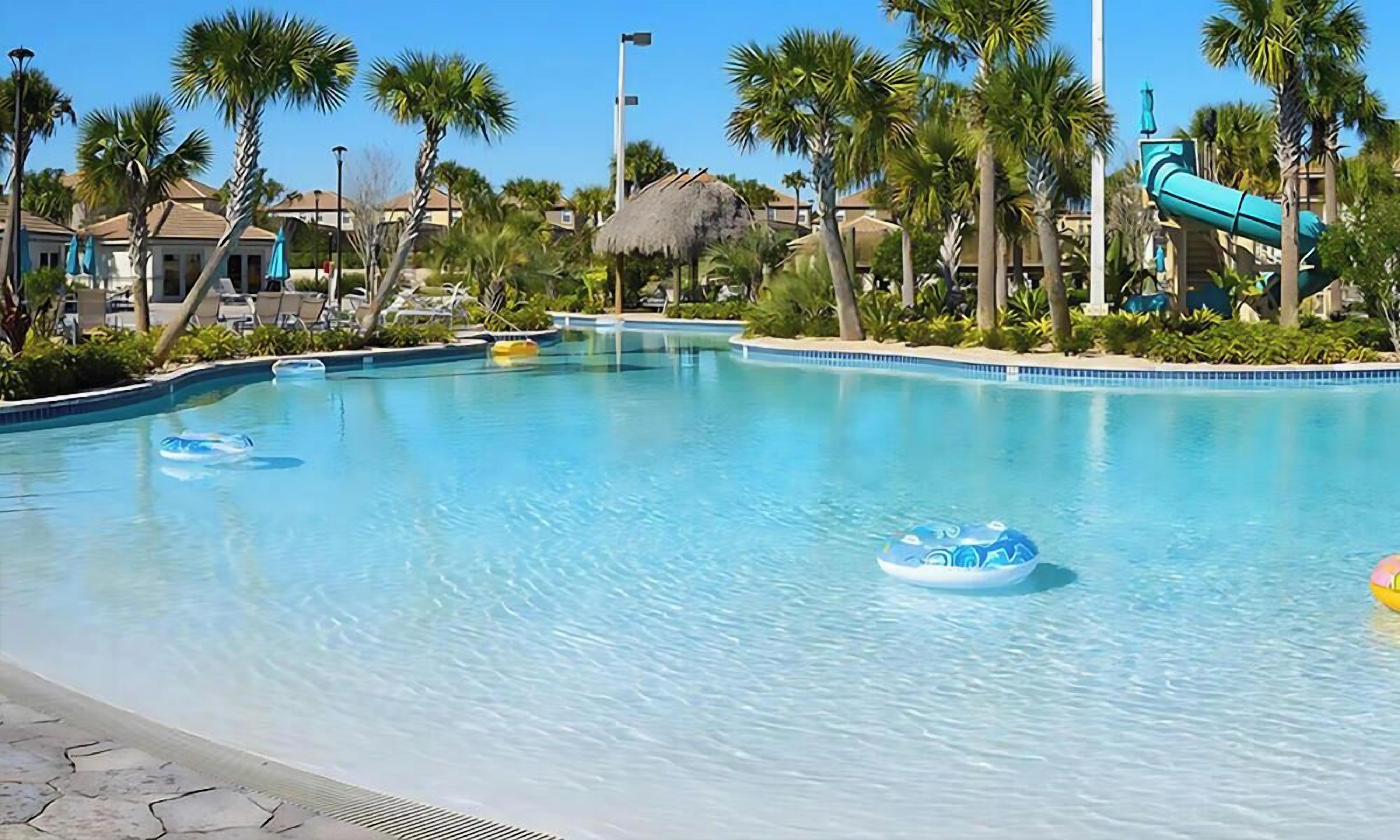 A clear swimming pool with lounge chairs and palm trees.