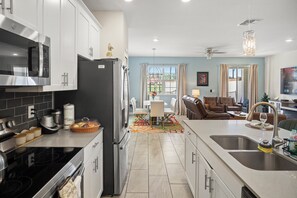 A modern kitchen with a central island, a dining area with a colorful rug, and a living space with a sofa and a TV. - 4BR/3BA Championsgate Villa With Private Pool (Davenport)