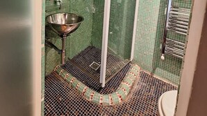 Ein Badezimmer mit grüner Fliesenwand, einem Metallwaschbecken, einer Duschkabine und einem Handtuchhalter.