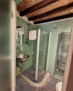 Ein Badezimmer mit grüner Fliesenwand, einem Metallwaschbecken, einer Duschkabine und einem Handtuchhalter.