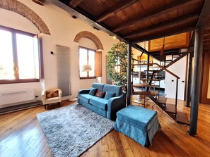 Ein Wohnzimmer mit blauem Sofa, grauem Teppich, Holzboden, einer Treppe und einer Pflanze.