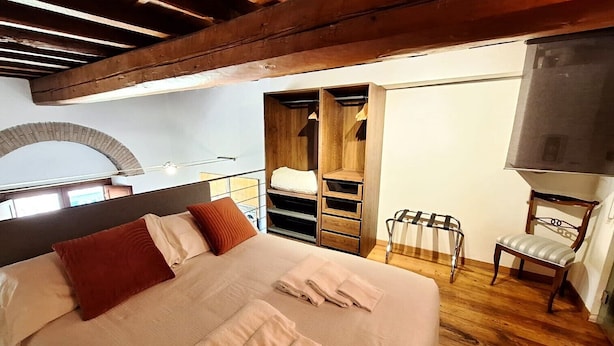 Ein Schlafzimmer mit einem großen Bett, Holzbalken, einem Kleiderschrank, einem Sessel und einem Fernseher.